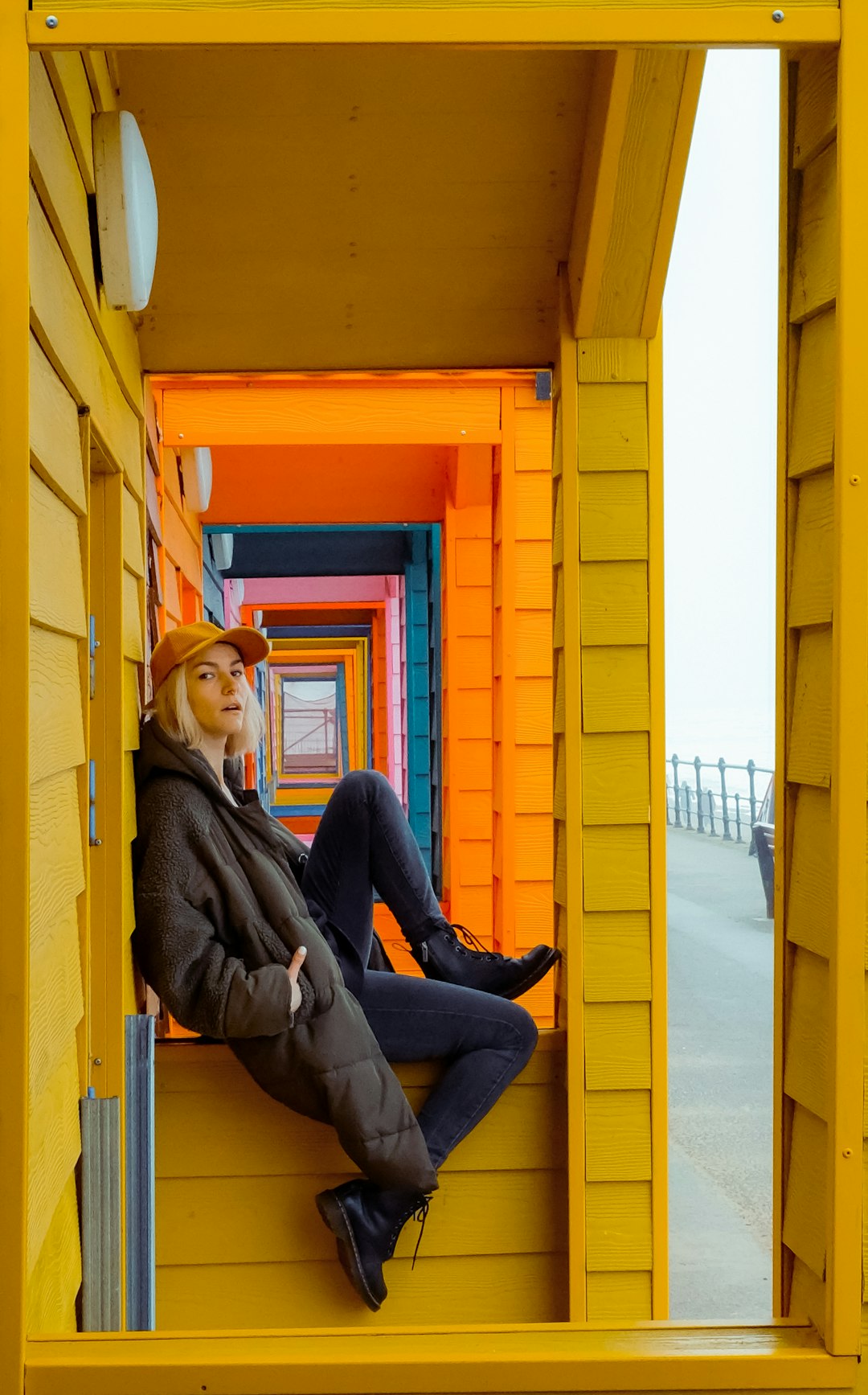 woman in brown jacket and blue denim jeans sitting on yellow wooden door during daytime tjpty9 3lsm